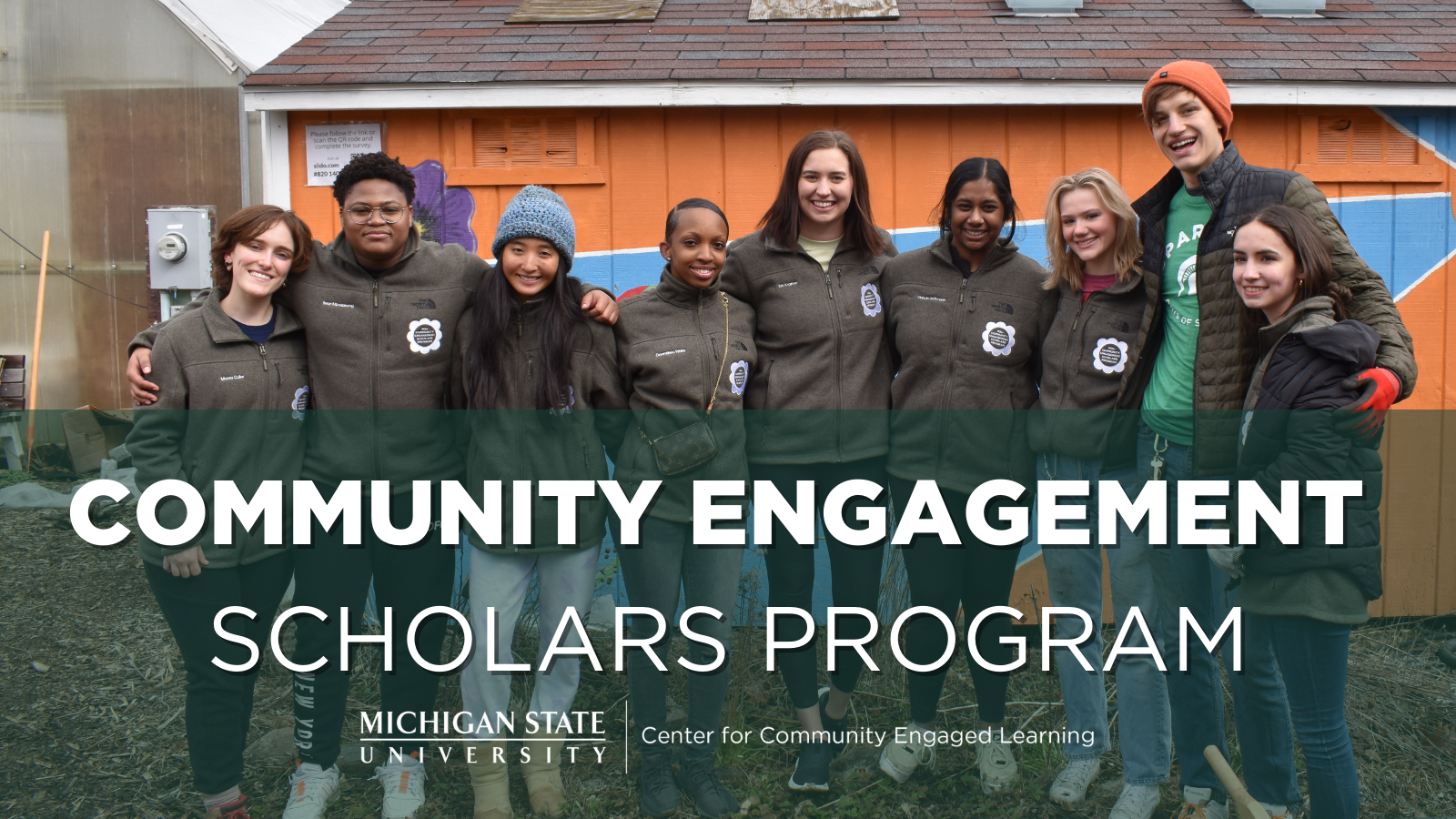 A group of young people in brown CESP jackets, smiling in front of a Community Engagement Scholars Program banner
